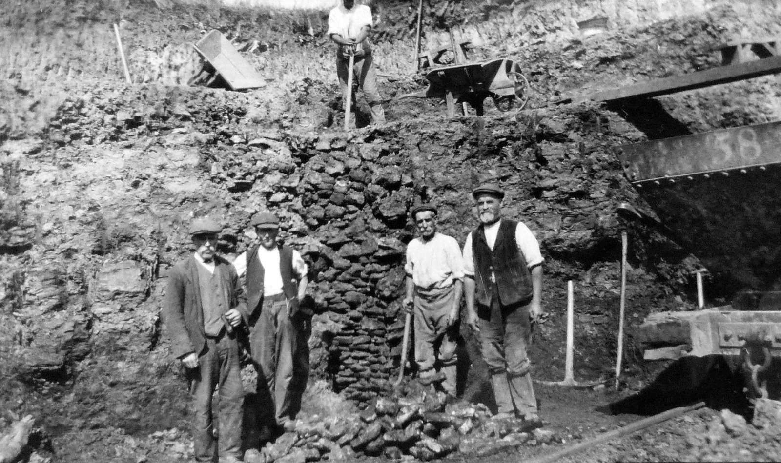 This photograph is labelled "Five men digging ironstone at Woodford House". On the back, the men are named (assuming names are as if looking at photograph). The Man with head cut off by photographer: J. Major (possibly Ringstead man James Major who was an ironstone labourer born in about 1850). and then from left: G. Saunders, G, Mayes, E. Manning, W. Riddle. With the kind permission Of Northamptonshire Record Office. Ch(H)127
